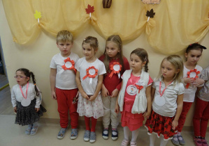 Siedmioro dzieci stoi w holu przedszkola. Wszystkie są ubrane w barwy narodowe z przyczepionymi do bluzek kotylionami.