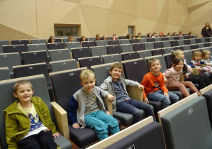 Czterech chłopców siedzi na fotelach i słucha koncertu w szkole Muzycznej