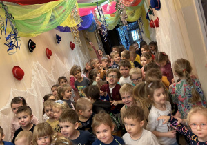 Duża grupa dzieci tańcząca na holu przedszkola przyozdobionym karnawałowo.