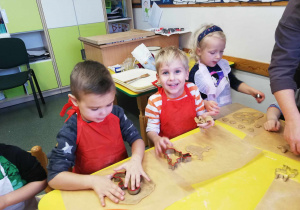 Dziewczynka i dwóch chłopców w czerwonych fartuszkach wyciskają z ciasta kształty pierników