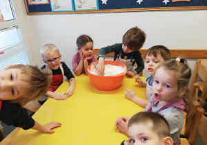 Dzieci mieszają mąkę w pomarańczowej misce.