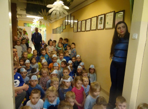 Dzieci ubrane na niebiesko siedzą w holu przedszkola