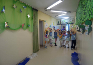 Dzieci ubrane na niebiesko tańczą w holu przedszkola mają uniesione nad głową ręce