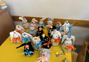 Na stole znajduje się dwadzieścia królików wykonanych przez dzieci. Króliki są w różnych kolorach z kokardką pod szyją.