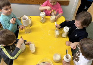 Dzieci siedzą przy stolikach i wsypują ryż do skarpet