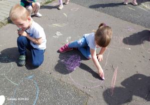 Dziewczynka i chłopiec rysują na betonowym boisku
