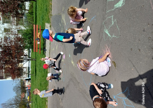 Grupka dzieci rysuje w różnych miejscach na asfalcie