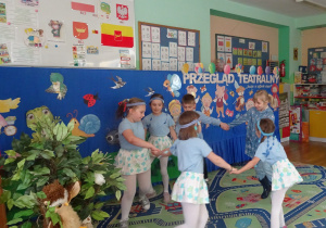 Dzieci ubrane na niebiesko tańczą w kole trzymając się za ręce.