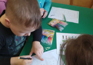 Dwoje dzieci siedzi przy stoliku i kolorowymi mazakami zaznaczają drogę dla robocika.