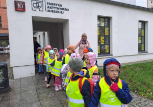 Na zdjęciu widać dzieci które stoją przed budynkiem Fabryki aktywności miejskiej.